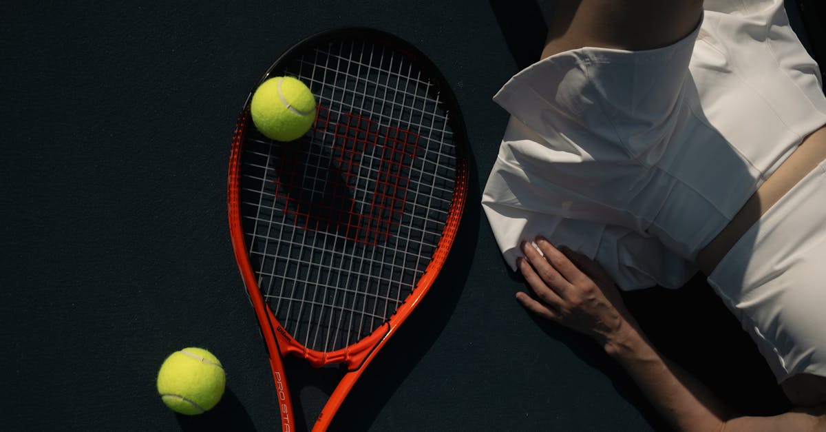 Tennis player in white sportswear next to racket and tennis balls on court.