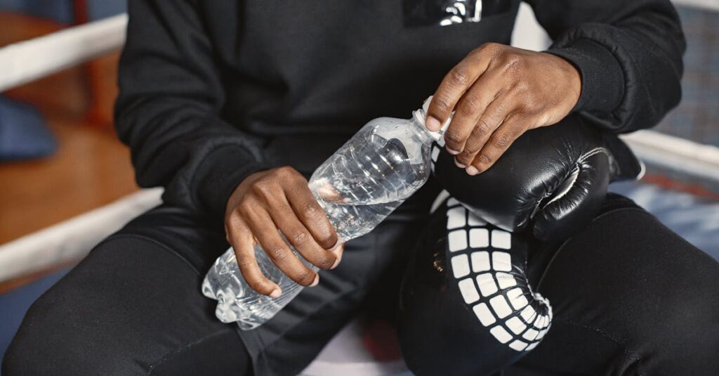 A boxer in black outfit holding a water bottle during a break indoors.